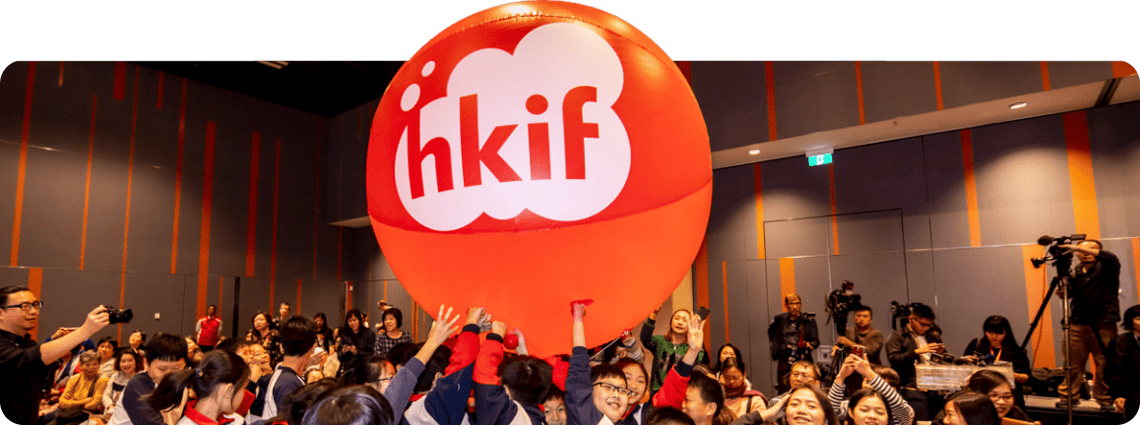 Community event with a large red HKIF balloon held up by children and adults in an auditorium